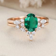 an emerald and white diamond ring on top of a cushioned surface with diamonds around it