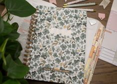 an open notebook sitting on top of a wooden table next to a potted plant