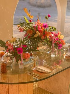 a glass table topped with lots of flowers and candles on top of it next to a window