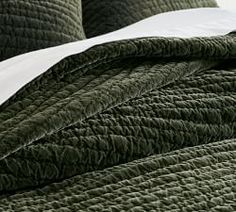 the bed is made with green quilts and pillows