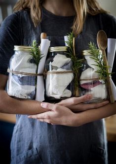 a woman holding four mason jars filled with food