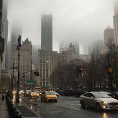 cars are driving down the street in front of tall buildings on a foggy day