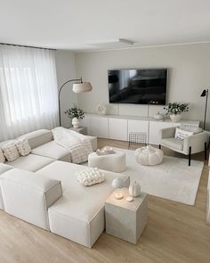 a living room filled with white furniture and a flat screen tv mounted on the wall