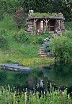 a small log cabin sitting on top of a lush green hillside next to a lake