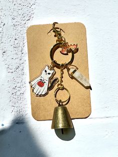 a keychain hanging on the side of a building with a bell and ghost charms attached to it