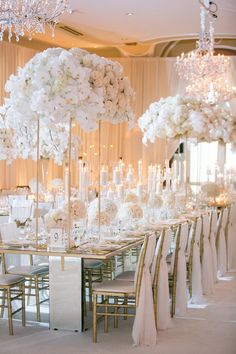 a long table with white flowers and chandeliers on the ceiling is set up for a formal function