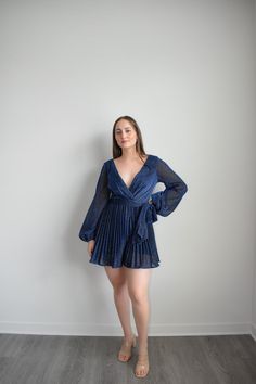 Navy Dress Romper with sparkling belt and long sleeves to dazzle at any formal event. Featuring an adjustable belt and a plunging v-neckline, you can elevate your look with sky-high heels or simply make it a more relaxed ensemble for at-home soirées. Crafted from a lightweight Polyester, this Navy Dress Romper is the epitome of grace and sophistication. Size guide: The First Model is 5'6" and wearing size Small. The Second model is wearing a size small Chic V-neck Dress With Belt, Elegant V-neck Belted Mini Dress, Elegant V-neck Belted Dress For Evening, Elegant Mini Belted Dress For Date Night, Glamorous Spring Evening V-neck Dress, Glamorous Long Sleeve V-neck Party Dress, Spring V-neck Belted Dress For Date Night, Fitted Party Dress With Belt, Glamorous Long Sleeve V-neck Dress For Date Night