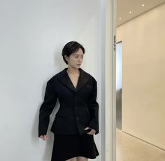 a woman standing in front of a white wall wearing a black jacket and skirt with one hand on her hips