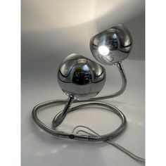 two chrome ball lamps on a white surface with a cord running through the middle and one lamp plugged in