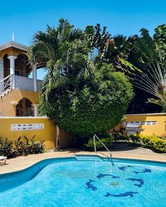 an empty swimming pool in front of a yellow house with palm trees and stairs leading up to the upper floor