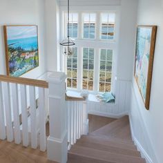 a staircase with white railings leading to two windows and paintings on the wall behind it