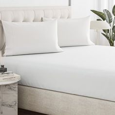 a bed with white sheets and pillows in a bedroom