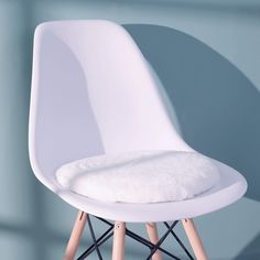 a white chair with wooden legs and a pillow on it's seat cushion in front of a blue wall