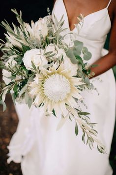 a bride holding a bouquet of flowers and greenery