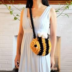 a woman wearing a white dress holding a black and yellow bag with a bee on it