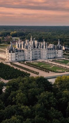 an aerial view of a large white building surrounded by trees and greenery at sunset