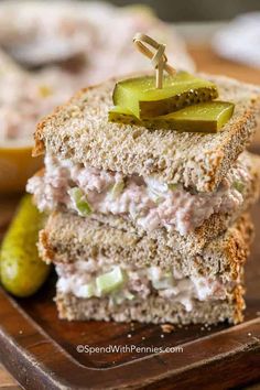 a close up of a sandwich on a cutting board with pickles in the background