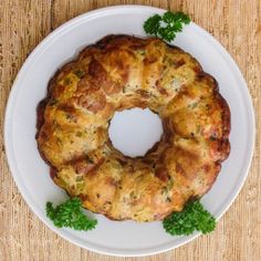 a white plate topped with a bundt cake covered in cheese and herbs on top of a wooden table