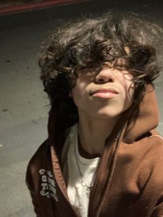 a young man with curly hair wearing a brown hoodie