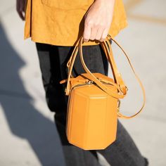 The cute Harper unexpected geometric shape gives this orange leather crossbody bag a playful but sophisticated runway savvy look. With its gold hardware, its small handle allows this orange leather bucket bag to swivel and be held in hand as a bucket. Its top zipper will keep your contents secure inside, while the cotton lined interior with 3 compartments keeps everything organized. This trendy designer crossover barrel bucket purse comes with a long and comfortable leather strap that can be flu African Accessories, Bucket Purse, Bucket Handbags, Mini Bucket Bags, Bag Dark, Mini Bucket, Dark Orange, Leather Bucket Bag, Leather Bucket