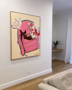 an abstract painting hangs on the wall next to a couch in a room with hardwood floors