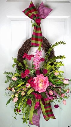 a wreath with pink flowers and greenery hanging on a door