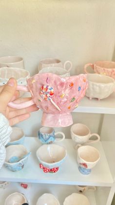 a person holding a pink heart shaped object in front of bowls and cups on shelves