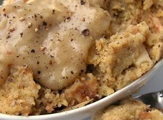 a white bowl filled with meat and gravy on top of a table next to a fork