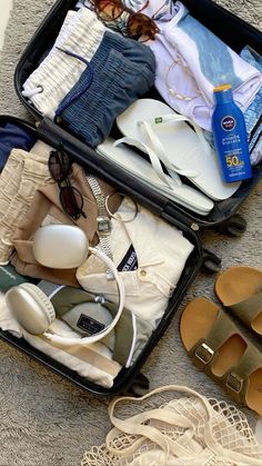 an open suitcase filled with clothing and shoes on the floor next to a pair of sandals