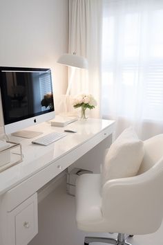 a white desk with a computer on it and a flower in a vase next to it