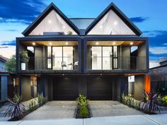 a large two story house with lots of windows and plants in the front yard at dusk