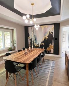 a dining room with a large wooden table surrounded by black chairs and lights hanging from the ceiling