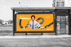 a bus stop with a large advertisement on it's side and a man holding a soccer ball in his hand