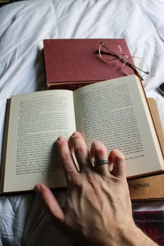 a person's hand resting on an open book next to a pair of glasses