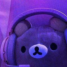 a teddy bear with headphones on sitting in front of a purple wall and looking at the camera