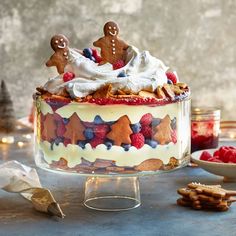 a cake decorated with gingerbreads, raspberries and other holiday treats sits on a table