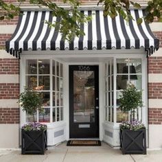 a black and white striped awning over the entrance to a store with potted plants