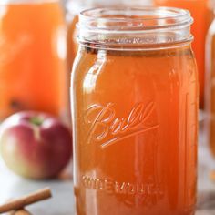 three jars filled with liquid sitting on top of a table next to apples and cinnamon sticks