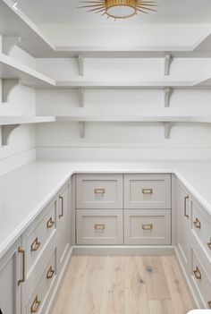 an empty walk in closet with white cabinets and gold handles on the doors, along with wooden flooring