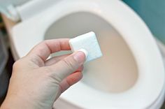 a hand holding a piece of toilet paper in front of a white toilet bowl with the lid up