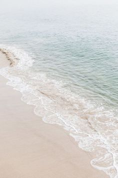 an empty beach next to the ocean with waves coming in and one person walking on it