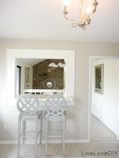 two white chairs sitting in front of a mirror on top of a wall next to a light fixture