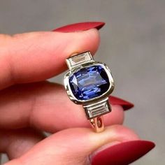 a woman's hand holding a ring with a blue stone in it