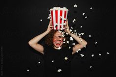 a woman holding a popcorn bucket over her head while she is surrounded by scattered popcorn