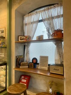 the shelves are filled with books and other items in front of a window that has sheer curtains