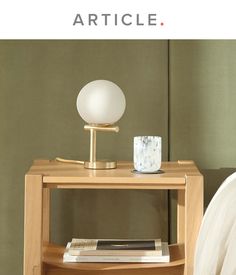 a table with a lamp on it next to a book shelf and a bed in the background