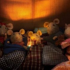 four stuffed mice are sitting on a bed with the lights turned on and one is holding a lit candle