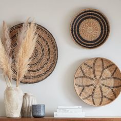 three woven baskets mounted on the wall above a wooden mantel with two vases