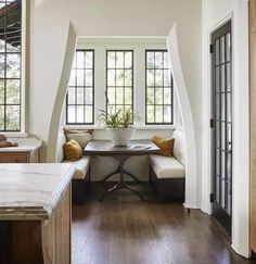 a kitchen with white walls and wood flooring next to a dining table in front of two windows