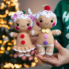 two small crocheted dolls are held in front of a christmas tree with lights